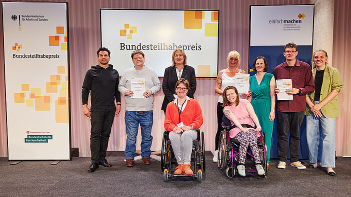 Die Gewinner*innen des Bundesteilhabepreises posieren mit Bärbel Bas, Bundesarbeitsministerin, auf der Bühne.