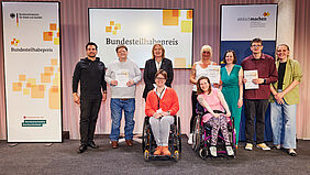 Die Gewinner*innen des Bundesteilhabepreises posieren mit Bärbel Bas, Bundesarbeitsministerin, auf der Bühne. 