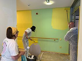 Mehrere Personen streichen eine Wand von grün zu gelb.
